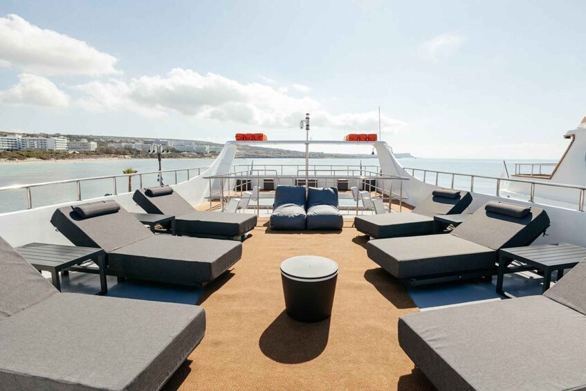 A sun deck with lounge chairs and a central ottoman on a boat. 1