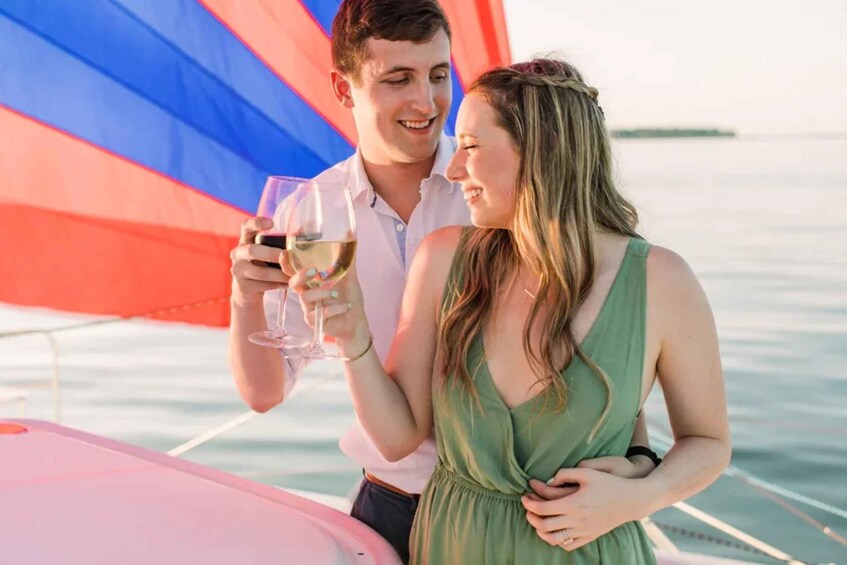 A couple on a sailboat with a red and blue sail, holding wine glasses. 2