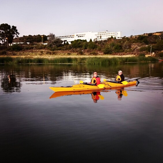 Two people kayaking on a calm lake with a building in the background. 3