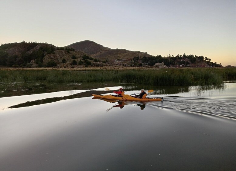 Two people kayaking on a calm river with a mountainous backdrop. 4