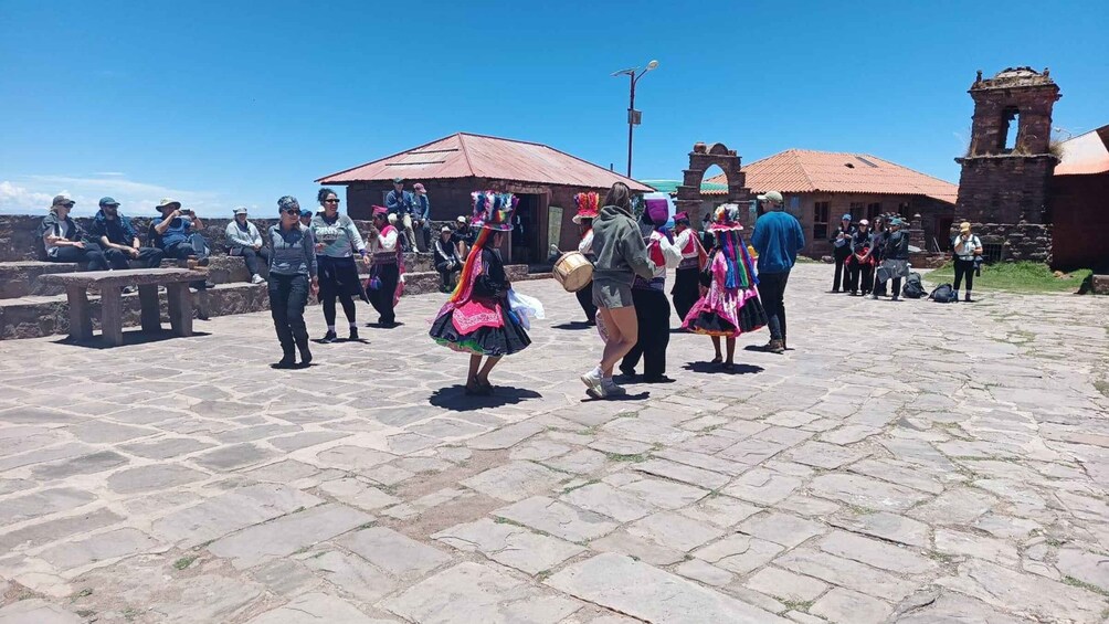 A group of people in traditional attire performing a dance on a cobblestone plaza with historic buildings in the background. 1