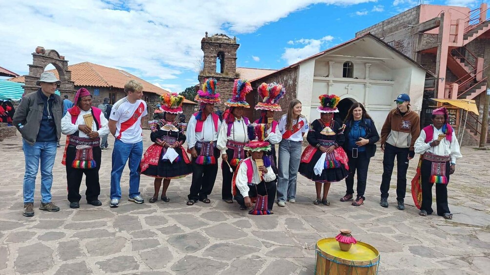A group of people in traditional attire standing in a plaza with a church and a stone tower in the background. 3