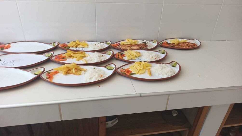 A kitchen counter with multiple plates of food, including rice, fried plantains, and vegetables. 4