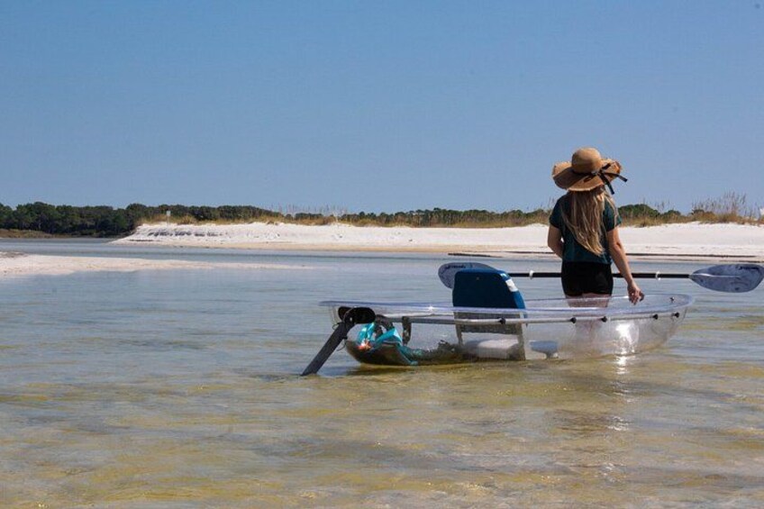 Eine Person in einem Boot auf ruhigem Wasser, mit sandigem Ufer und vereinzelter Vegetation im Hintergrund. 2