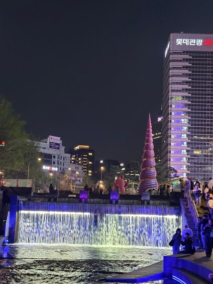 A nighttime cityscape with a water feature, a tall spire, and illuminated buildings. 1