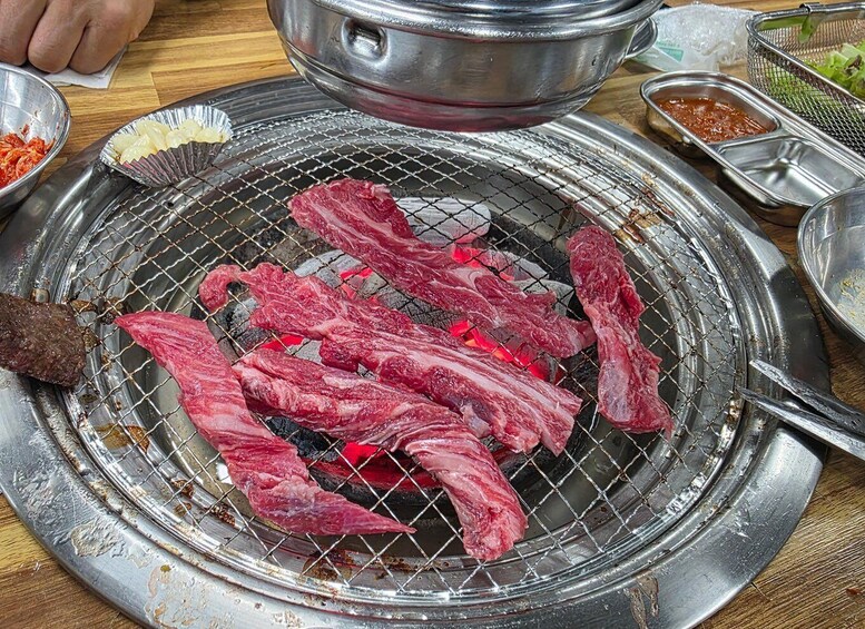 Raw meat on a grill with charcoal, a metal bowl, and a container of sauce. 4