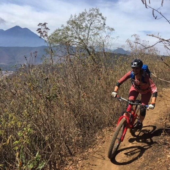 A mountain biker on a trail with sparse vegetation and a mountain in the background. 2