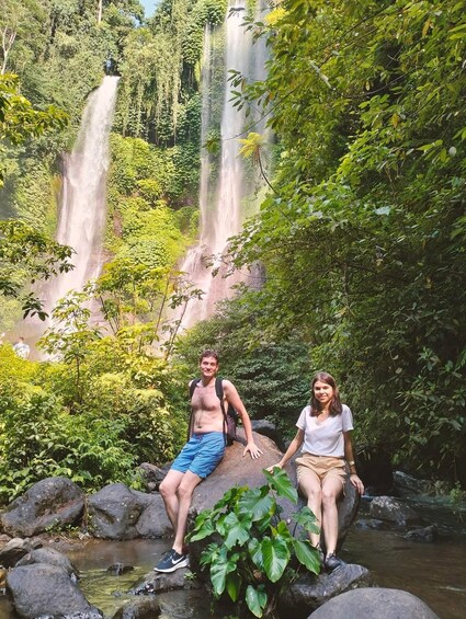 Two people sitting on rocks by a waterfall in a lush forest. 3