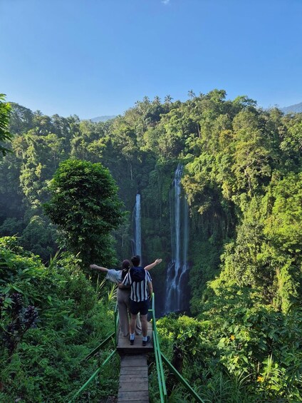 A couple on a wooden bridge overlooking a waterfall in a lush forest. 1