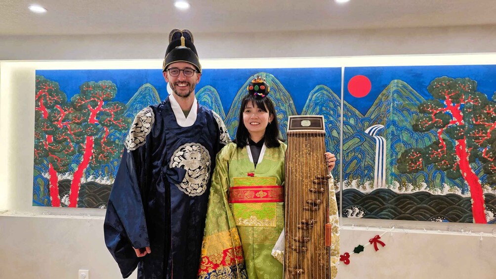 Two people in traditional attire, a painting of a mountainous landscape, and a traditional stringed instrument. 5