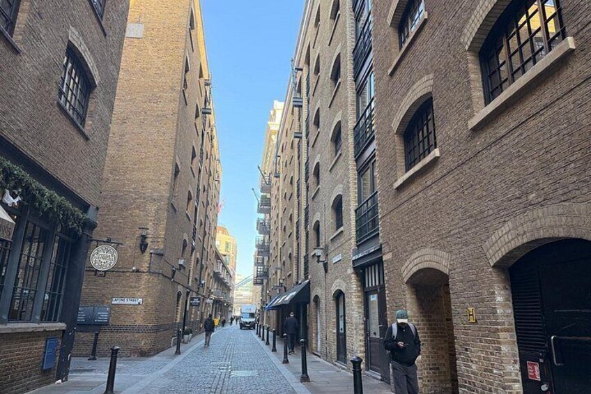 A cobblestone street lined with brick buildings, a clear blue sky, and a person walking away from the camera. 2