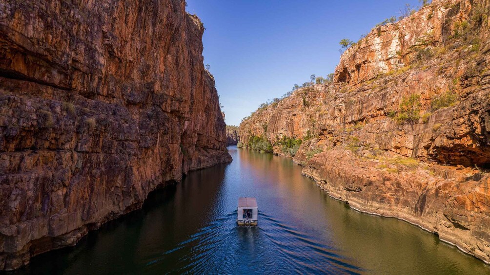 A narrow canyon with steep red rock walls and a boat navigating the calm waters. 2