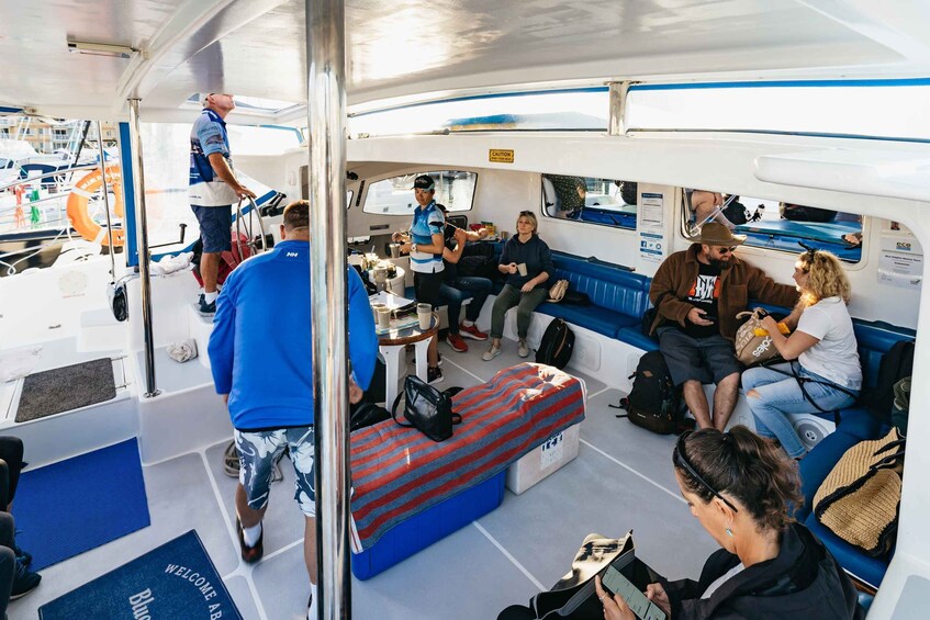 A boat interior with people seated, a man standing, and a bench with a striped blanket. 5