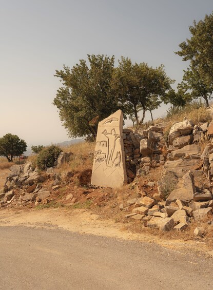 A stone monument with carvings of a man, a dog, and a cat, surrounded by rocks and trees. 4