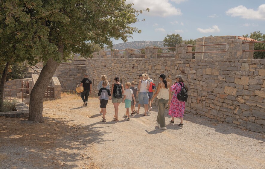A group of people walking along a stone pathway in a historical site with a tree and a stone wall in the background. 5