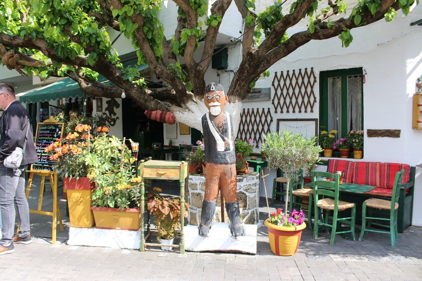 A statue of a man in a hat and boots, a tree, and a café with outdoor seating. 2