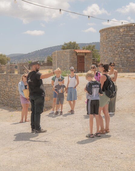 A group of people standing on a gravel path near stone walls and a building with a tiled roof, under a clear sky. 3