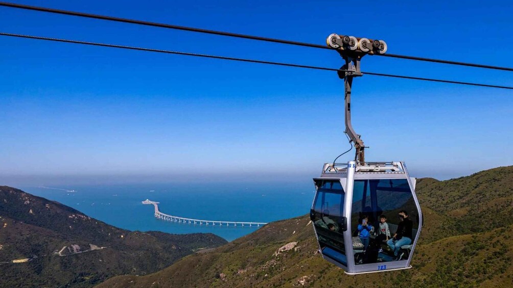 A cable car suspended over a mountainous landscape with a bridge in the distance. 2