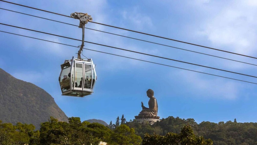 A cable car with passengers, a large Buddha statue, and a mountainous landscape. 3