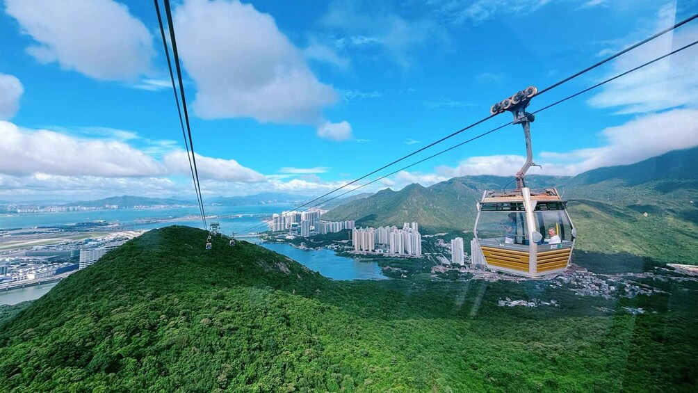 A cable car system with a lush green hill, a river, and a cityscape in the background. 1