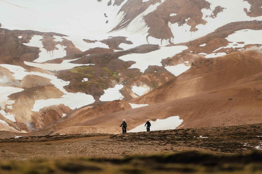 Two hikers on a rocky terrain with patches of snow. 5