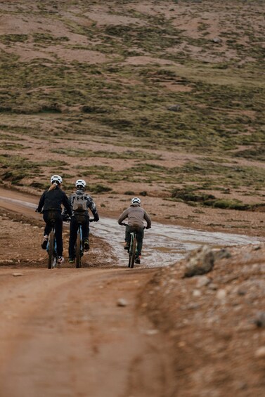 Three cyclists on a dirt road in a hilly, barren landscape. 3