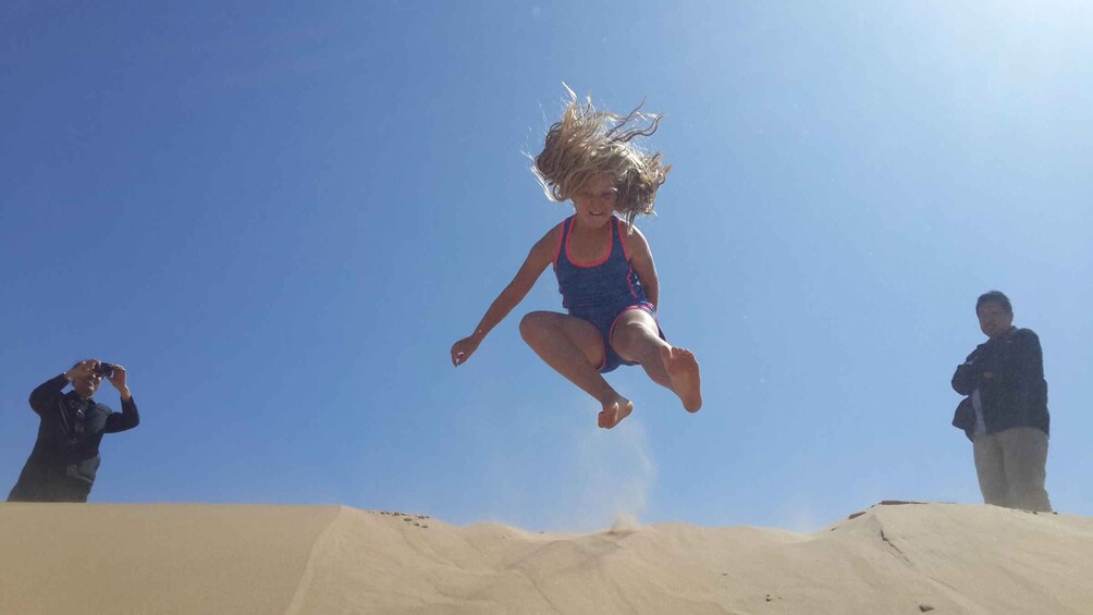 A person jumping off a sand dune, with a clear blue sky in the background. 4