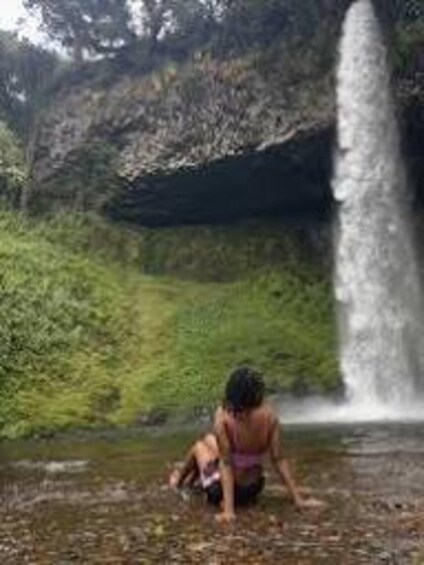 A person crouching near a waterfall in a forested area. 5