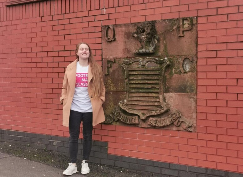 A person standing in front of a red brick wall with a coat of arms. 2