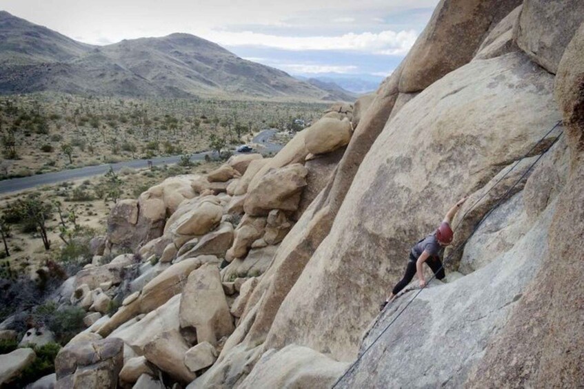 A person rock climbing a large boulder in a desert landscape with mountains in the background. 5