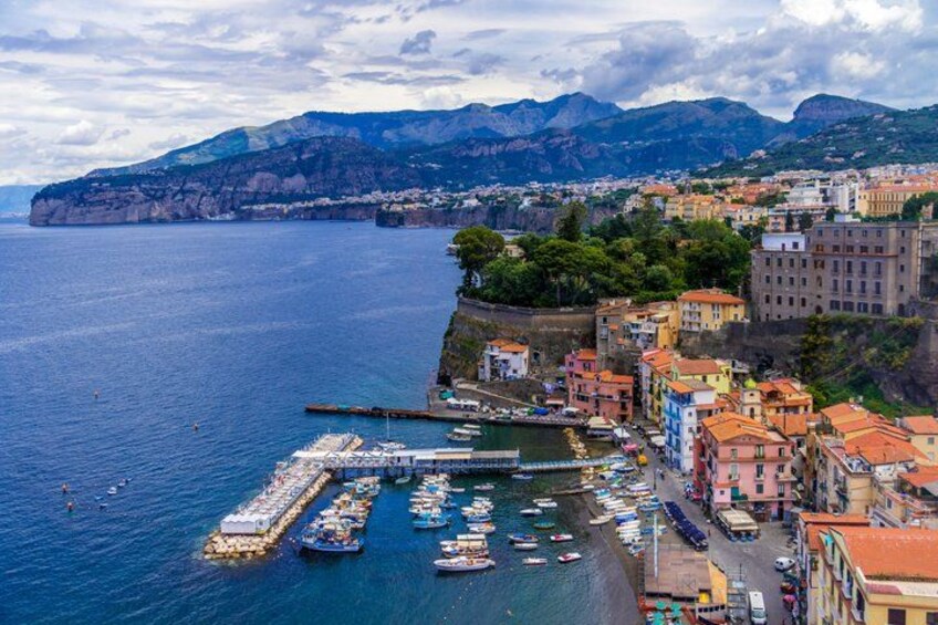 A coastal town with a marina, colorful buildings, and mountains in the background. 2