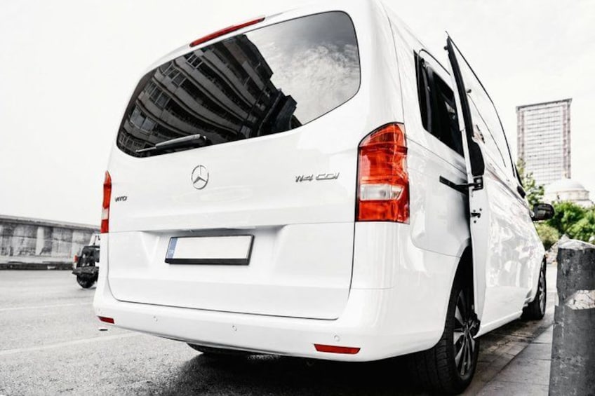 A white Mercedes-Benz Sprinter van parked on a road with a cityscape in the background. 1