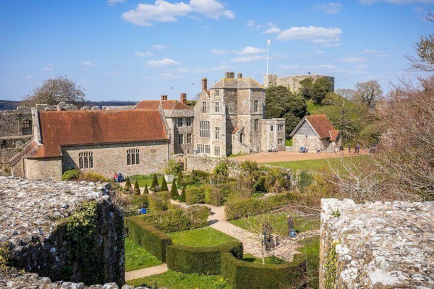 A historic stone building with a tower, surrounded by well-maintained hedges and a clear sky. 1