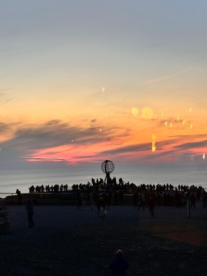 A sunset over a beach with people gathered, a Ferris wheel, and a clear sky. 3