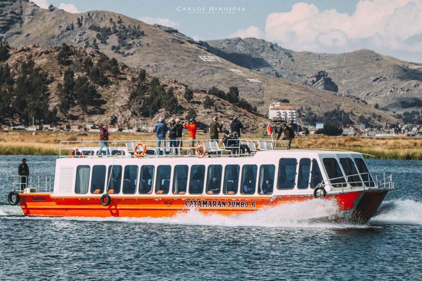 A boat named 'CATAMARAN JUMBO G' on water with passengers and a mountainous landscape in the background. 2