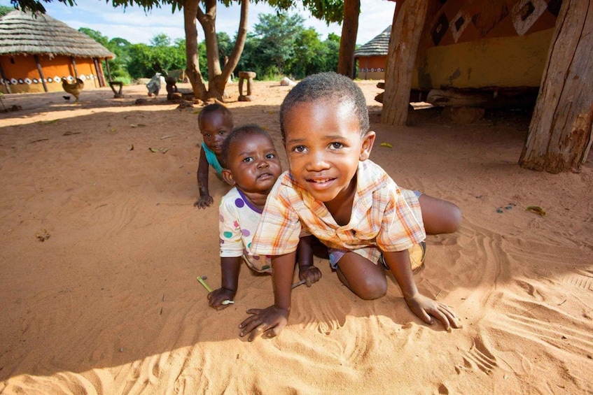 Children playing in a sandy area with huts in the background. 3
