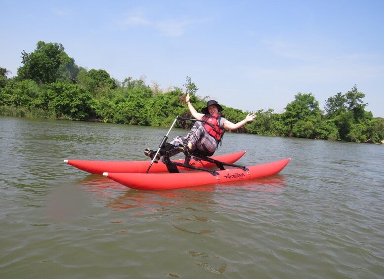 A person kayaking on a red kayak with a life jacket, surrounded by calm water and greenery. 4