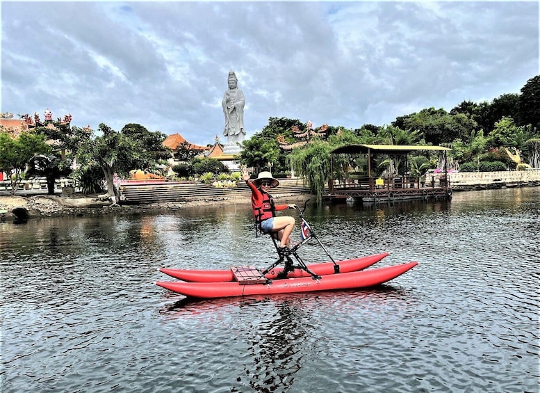 A person on a red kayak in a calm body of water with a statue and traditional architecture in the background. 3