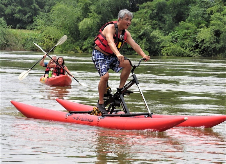 A person on a red kayak with a paddle, another in a red inflatable boat, surrounded by greenery. 1