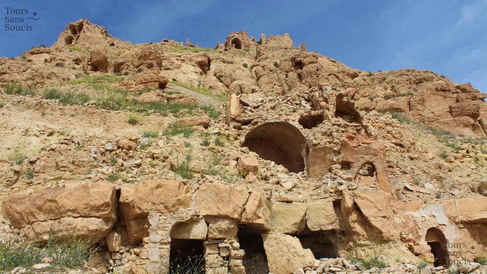 Ancient ruins with multiple cave-like structures and arches on a rocky hillside. 4