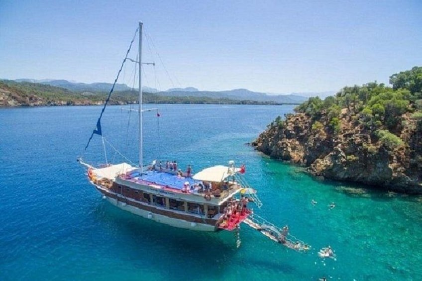 A boat anchored near a rocky coastline with clear blue water. 1
