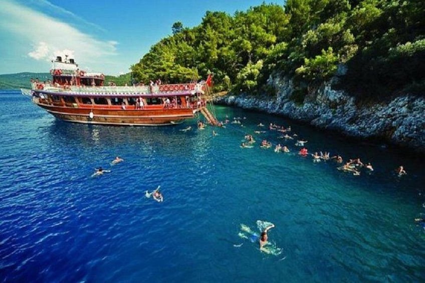 A boat with people swimming in the water and a rocky coastline. 2