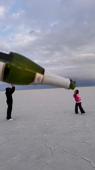 Two people in a barren landscape with a large bottle of champagne being tilted. 4