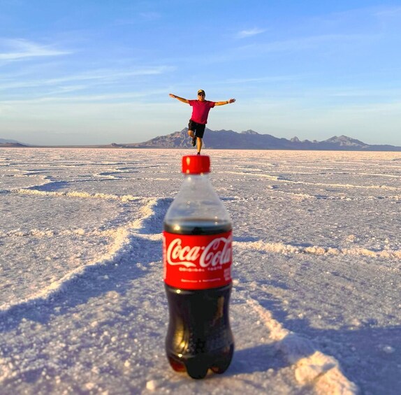 A person standing on a frozen landscape with mountains in the background and a Coca-Cola bottle in the foreground. 3