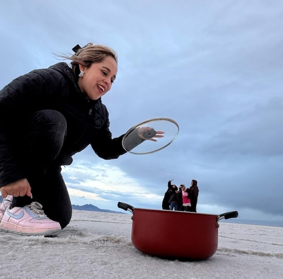 A person crouching by a red pot on a salt flat with a cloudy sky. 1
