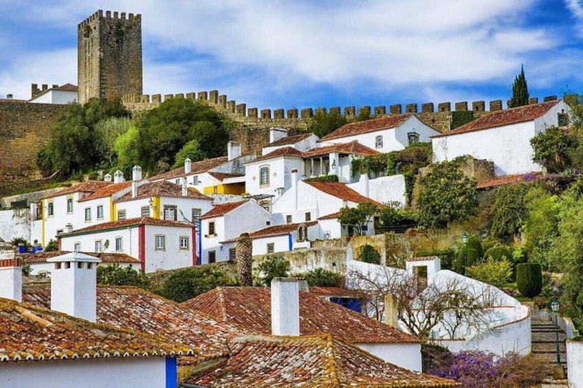 Un pueblo histórico con edificios blancos, una torre destacada y una colina con muralla defensiva. 2