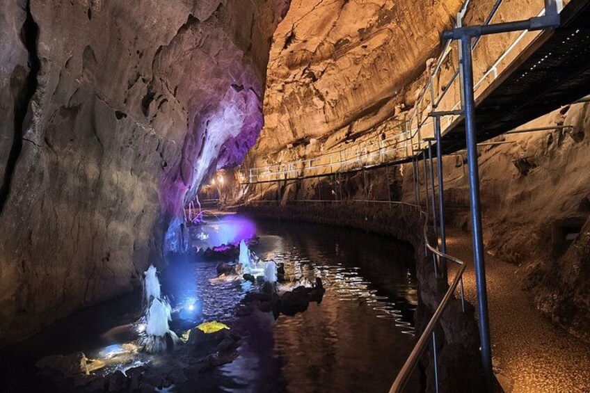 Una cueva con formaciones de agua, un pasillo de metal y una luz púrpura. 3