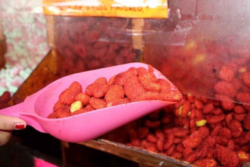 En rosa ske fyldt med røde snacks holdes over en beholder med lignende snacks. 5