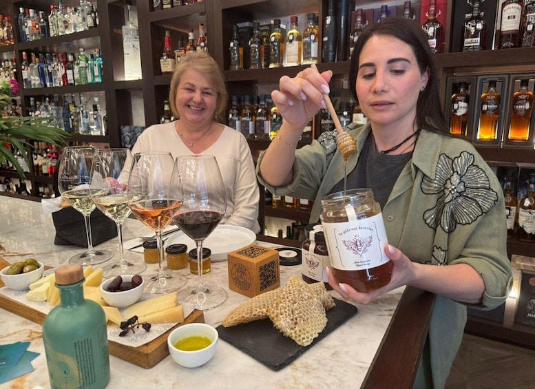 Two people tasting honey at a bar with wine glasses and honey jars on the table. 1