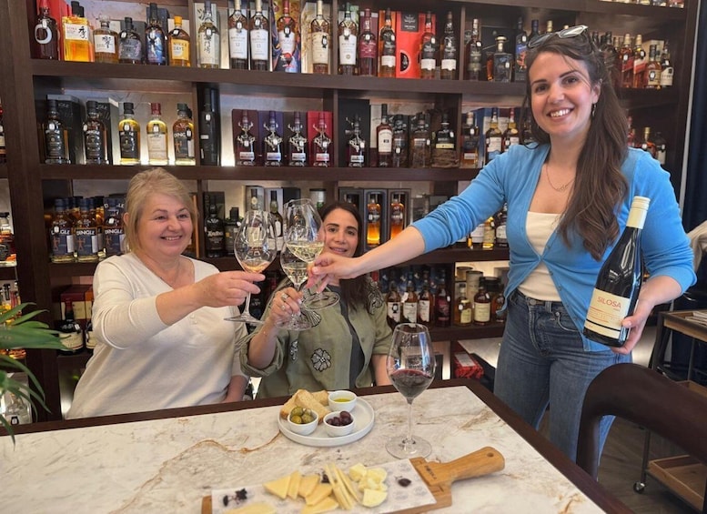 Three people toasting with wine glasses in a bar with shelves of liquor bottles. 3